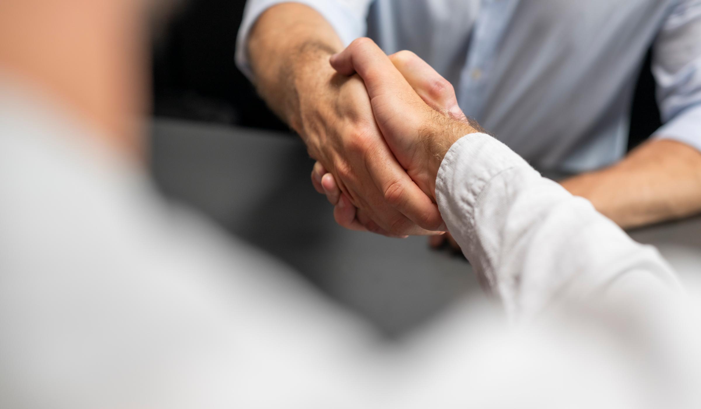 Über-die-Schulter-Perspektive auf Handschlag zwischen zwei Männern